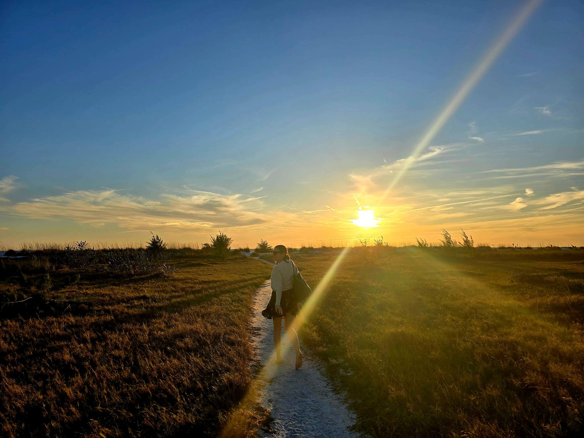 A figure walking along the shore at sunset.